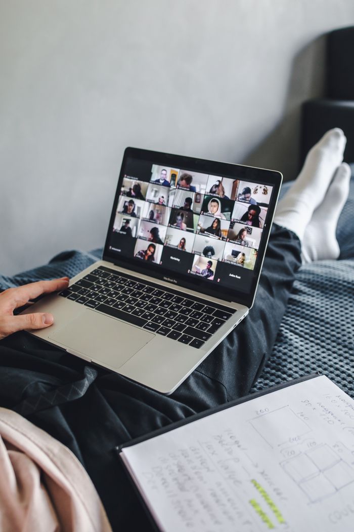 Crafting Captivating Headlines: Your awesome post title goes here Adult sitting on bed using laptop for video conference and note-taking.