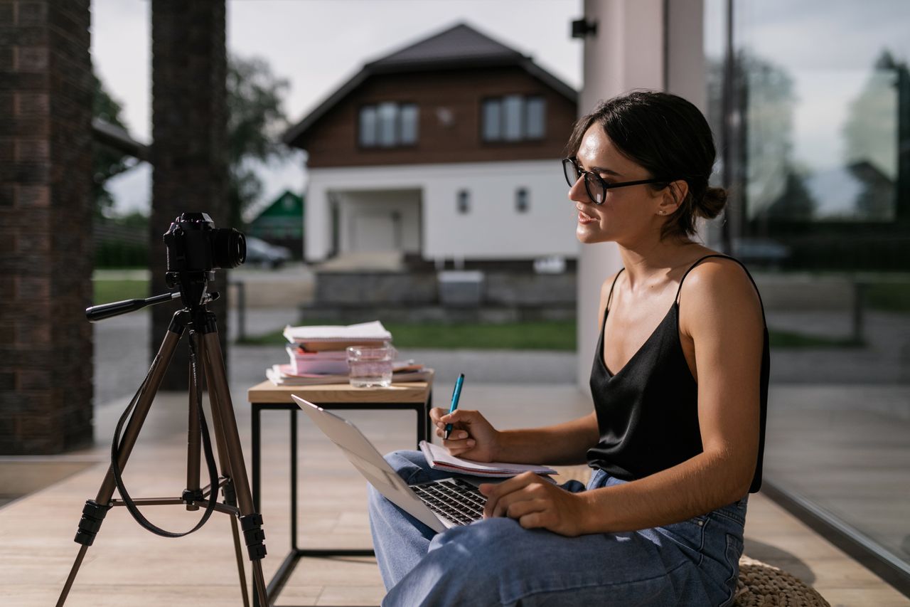 Woman sitting with laptop taking notes for an online class, intense focus outdoors.